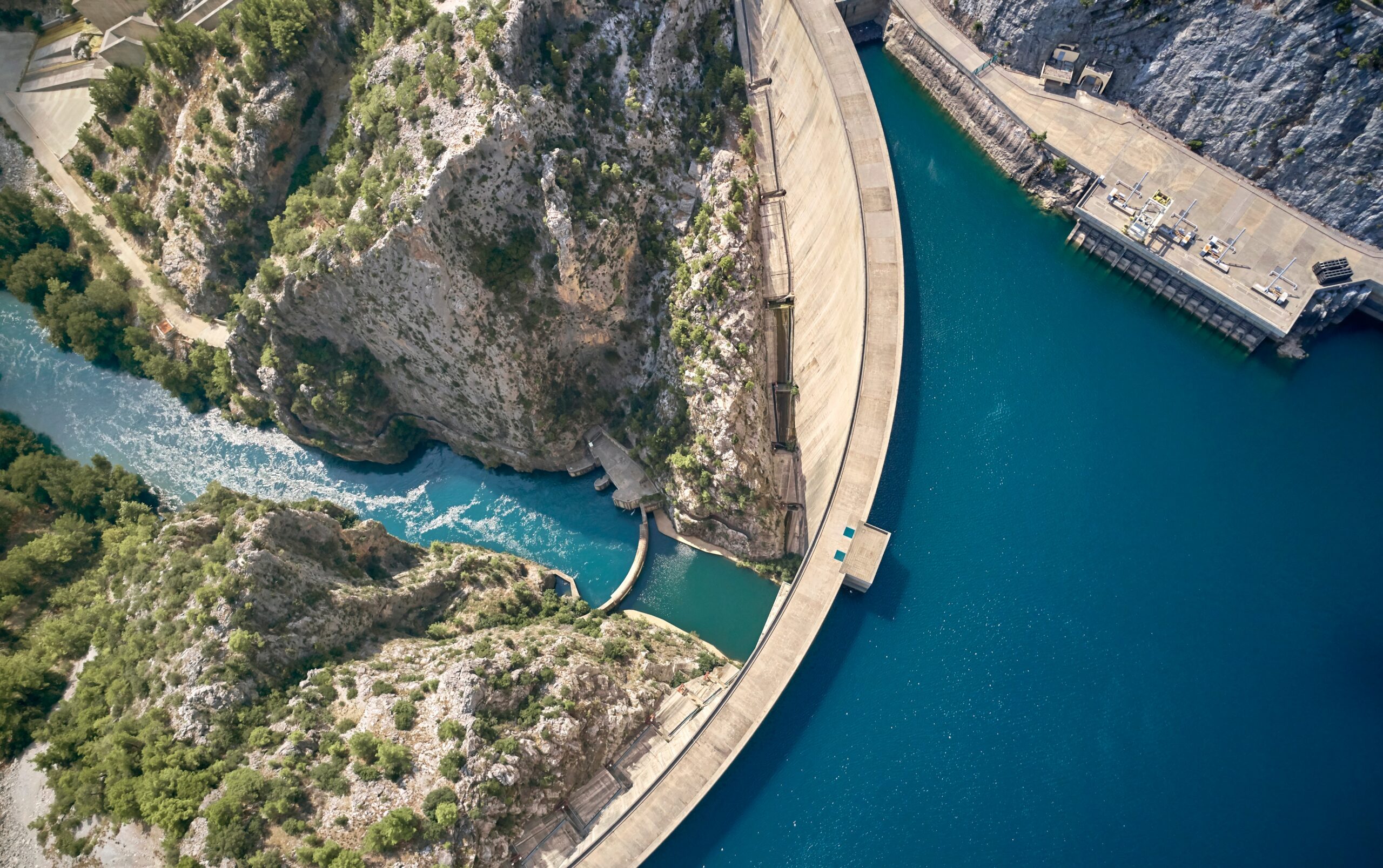 Luftaufnahme einer Staumauer zwischen felsiger Landschaft und einem Stausee