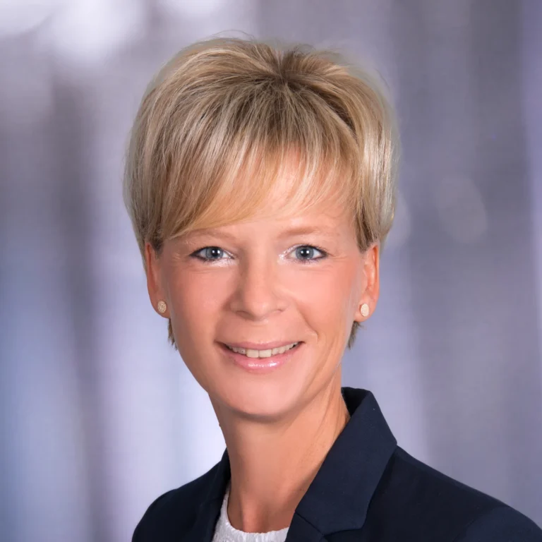 Porträt einer lächelnden Mitarbeiterin vor neutralem Hintergrund.